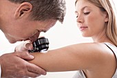 Doctor examining mole on young woman's arm