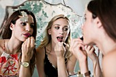 Young women applying lipstick in mirror