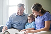Boy reading a book with his grandfather and his mother