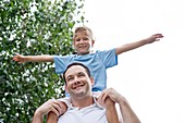 Father carrying son on shoulders with arms out