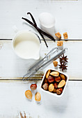Dough recipe ingredients (egg, milk, sugar, nuts, vanilla and cinnamon sticks) on white wooden background