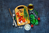 Tasty vegetarian ingredients, olive oil and seasoning on rustic wooden cutting board over dark vintage background