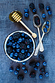 Harvest background with dark berries in vintage spoons and honey over grunge table