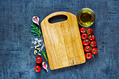 Top view of empty vintage cutting board with organic tomatoes, spices and olive oil over dark grunge background