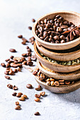Variety of different coffee beans and spices in wooden bowls in stack over grey table