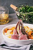 Sous vide sliced rack of lamb with sauce and backed sweet potatoes served in ceramic plate with green salad and white wine