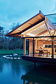 Woman sitting at table in illuminated architect-designed house on lake