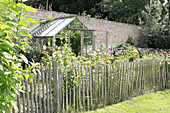 Paling fence surrounding cottage garden with greenhouse