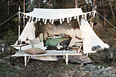 Feldbett und Stühle vor eingerichtetem Zelt mit Lichterkette