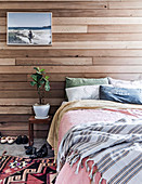 Doppelbett und Nachttisch mit Zimmerpflanze vor Wandverkleidung aus recyceltem Zedernholz