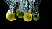Lemons and limes falling in water, slow motion