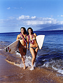 Two women wearing bikinis on the beach with surfboards