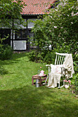 Alter Schaukelstuhl mit Decke und Kissen und Tischchen im Garten