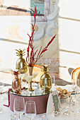 Verspiegeltes Podest mit Vase, Kerzen und goldener Ananas auf festlich gedecktem Tisch
