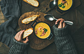 Winterlich gekleidete Frau isst Maiscremesuppe mit Garnelen und Röstbrot (Aufsicht)