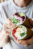 Sushi burritos being held in a persons hands