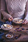 Woman eating apple buckwheat porridge topped with walnuts, cashew butter, apples slices and cacao nibs