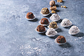 Variety of homemade dark chocolate truffles with cocoa powder, coconut, walnuts over blue texture background
