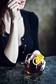 Junge Frau sitzt mit Cocktail an Bartheke