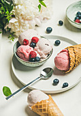Pink strawberry and coconut ice cream scoops in bowl, sweet cones, peony flowers bouquet and fresh berries
