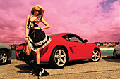 A blonde woman wearing a summer dress standing by a red car