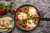 Shakshuka in an iron pan with pita bread, paprika, tomatoes and parsley
