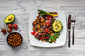 A salad plate with smoked tofu, chard, chickpeas, avocado, black sesame, tomatoes, mangetout and sprouts