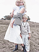 A blonde woman wearing a sleeveless jumper and a white skirt with two children