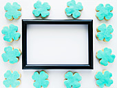 A black picture frame surrounded by clover-shaped cookies