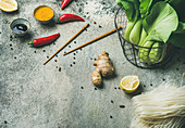 Asian cuisine ingredients over grey concrete background, copy space, vegetables, spices, noodles, sauces for cooking vietnamese, thai or chinese food