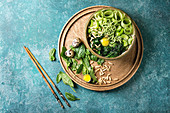 Ceramic bowl with vegetarian green pea noodles, sliced cucumber, celery, spinach, quail egg yolk, pine nuts with wooden chopsticks