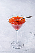 Roter Kaviar mit Löffel in Cocktailglas vor weißem Hintergrund