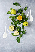 Detox drink concept. Ingredients for smoothie green spinach leaves, apple, orange, yogurt splash over gray texture background