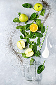 Detox drink concept. Ingredients for smoothie green spinach leaves, apple, orange, yogurt splash, mason jar, cocktail tube over gray texture background