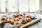 Homemade Easter traditional hot cross buns on wooden tray with textile over white wooden table