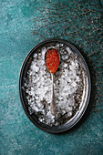 Spoon of red caviar on vintage metal tray with ice over turquoise texture background