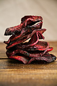 Organic homemade beetroot chips cooked in oven with olive oil, pepper and salt lying in a stack on wooden table