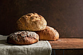 A variety of rustic bread loaves on a linen and a rich, wood surface