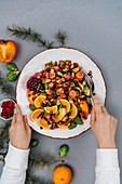 A woman serving a bowl of roasted brussels sprouts salad with carrot, orange, persimmon and pomegranate