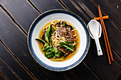 Ramen asian noodle in broth with Beef and pak choi cabbage in bowl on dark wooden background