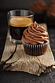 Dark chocolate cupcakes with ganache frosting on dark background with espresso in a glass