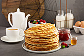 Big stack of homemade crepes or thin pancakes with butter, jam and honey