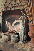Dog figurine and old stone pots in front of painting of woman