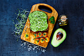 Fresh vegetarian sandwich with whole grain bread, alfalfa and guacamole on rustic wooden cutting board over dark vintage background