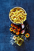 Pasta ingredients background: Dry pasta with olive oil, garlic, spices and tomatoes on dark vintage table