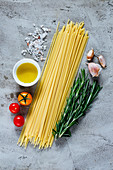Italian spaghetti, tomatoes, olive oil and rosemary, ingredients for cooking over grey concrete background