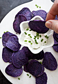 A woman s hands dipping a purple chip into tzatziki dip with chopped chives