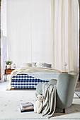 Armchair and box spring bed with blue and white gingham frame in front of long curtains