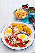 Huevos Motuleños (fried eggs on a tortilla with black bean puree, chilli sauce, plantains, bacon and cheese, Mexico)