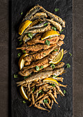 Assortment of fried fish with lemon wedges and parsley on slate plank and dark background